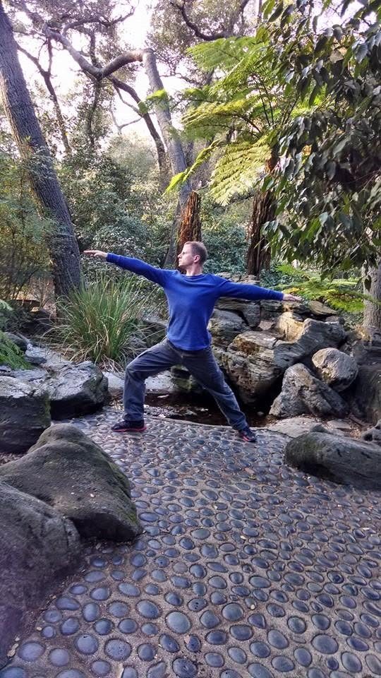 David DuVal in warrior two yoga pose in a fern garden