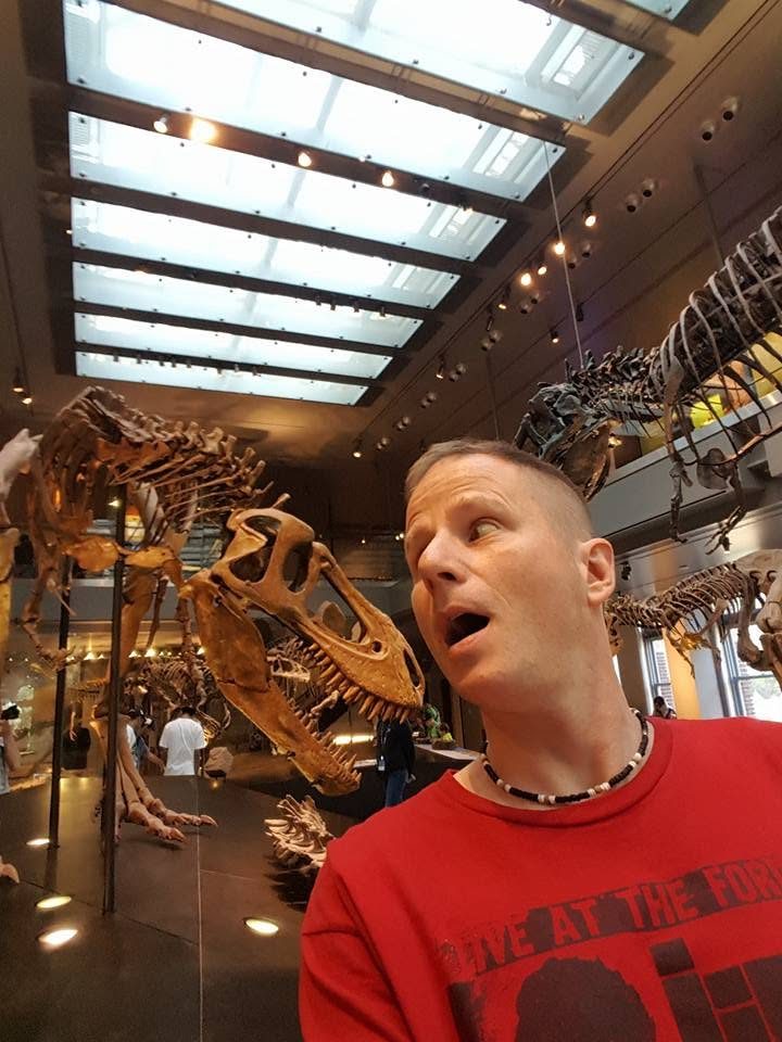 David DuVal making a surprised face beside dinosaur skeletons at a natural history museum in Los Angeles