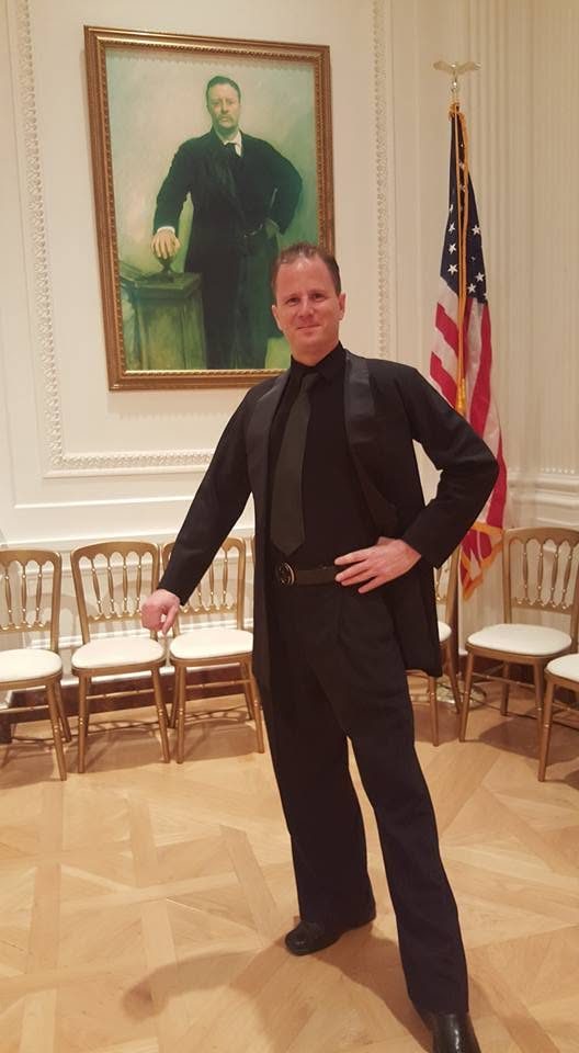David DuVal in a tuxedo at the Nixon Library, standing before a portrait and an American flag